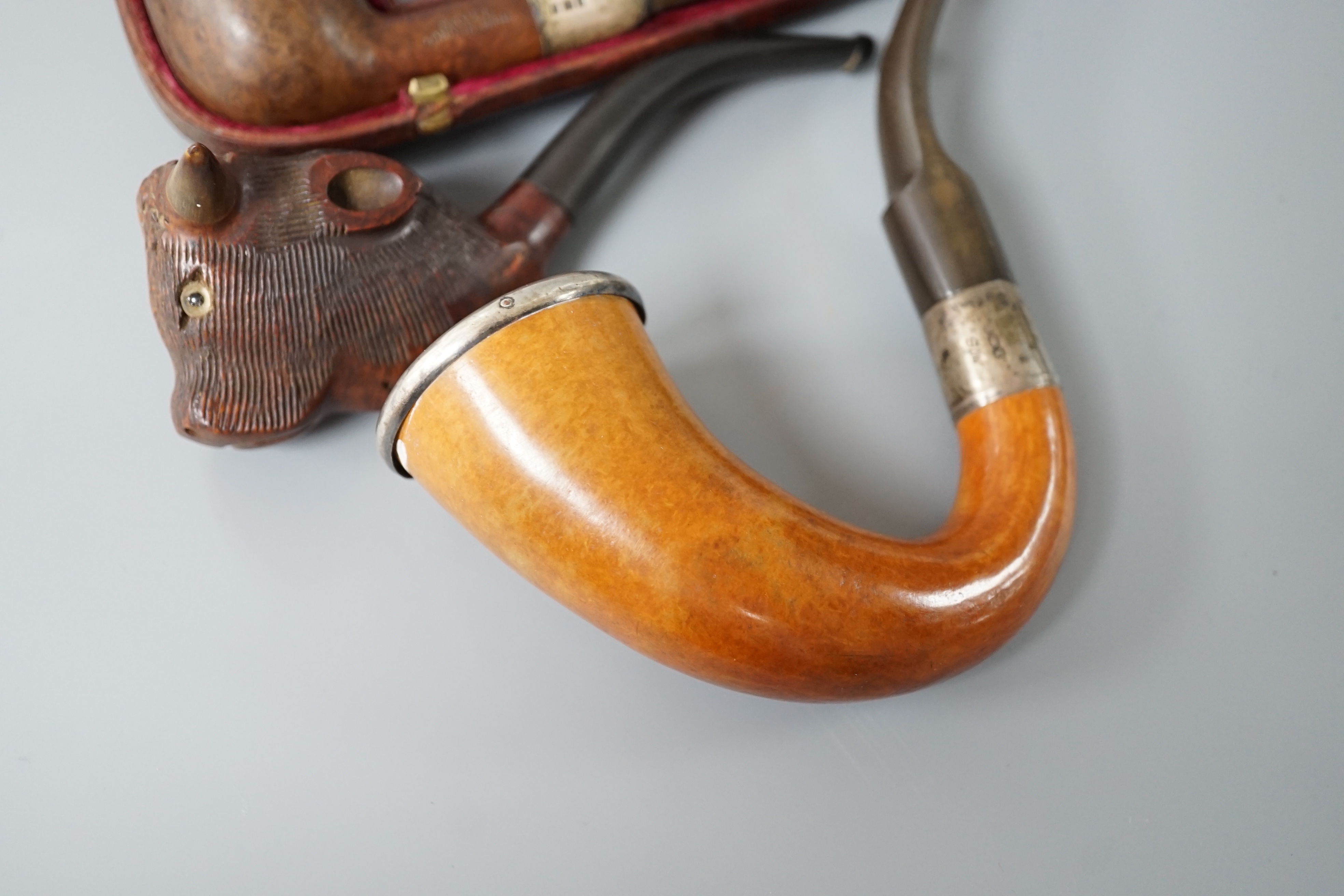 A cased Savel burr wood smokers pipe with silver collar, another pipe with silver collar and rim together with a novelty carved wood and horn ‘cow’ pipe